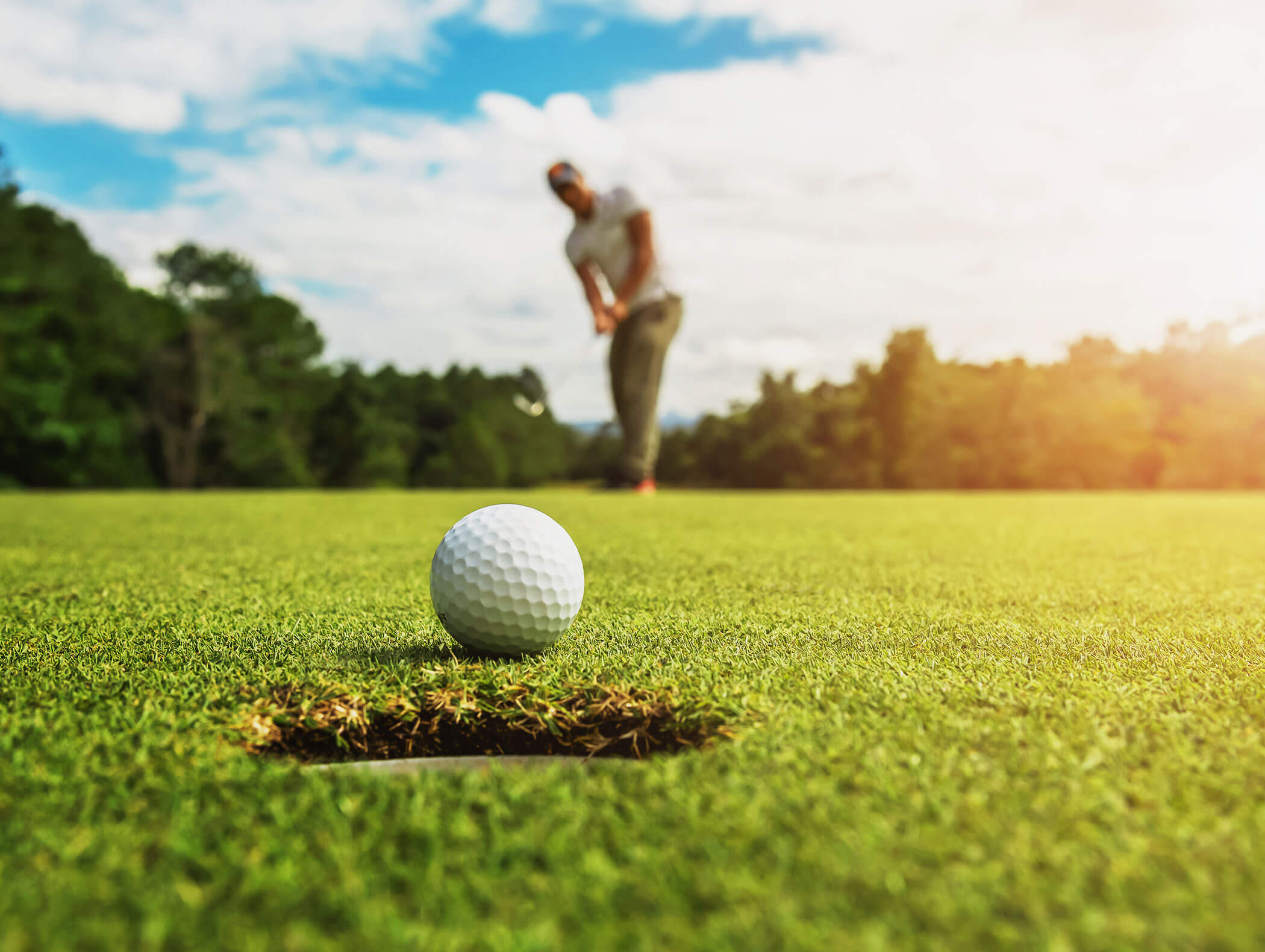 Golfball liegt vor dem Loch, dahinter unscharf der Golfspieler - Hotel Montis