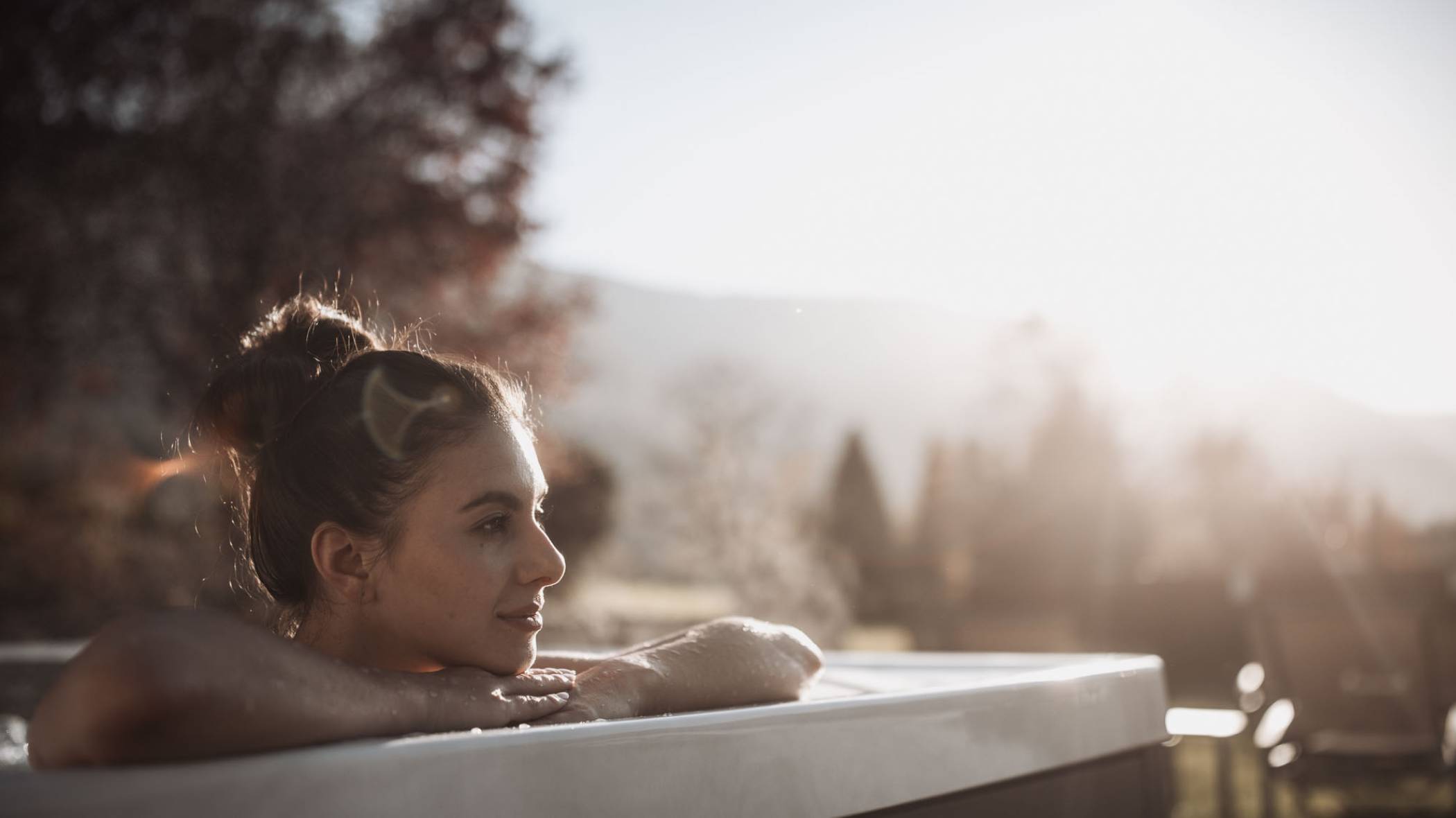 Eine Frau sitzt im Outdoor-Whirlpool und blickt in die Ferne - Hotel Montis