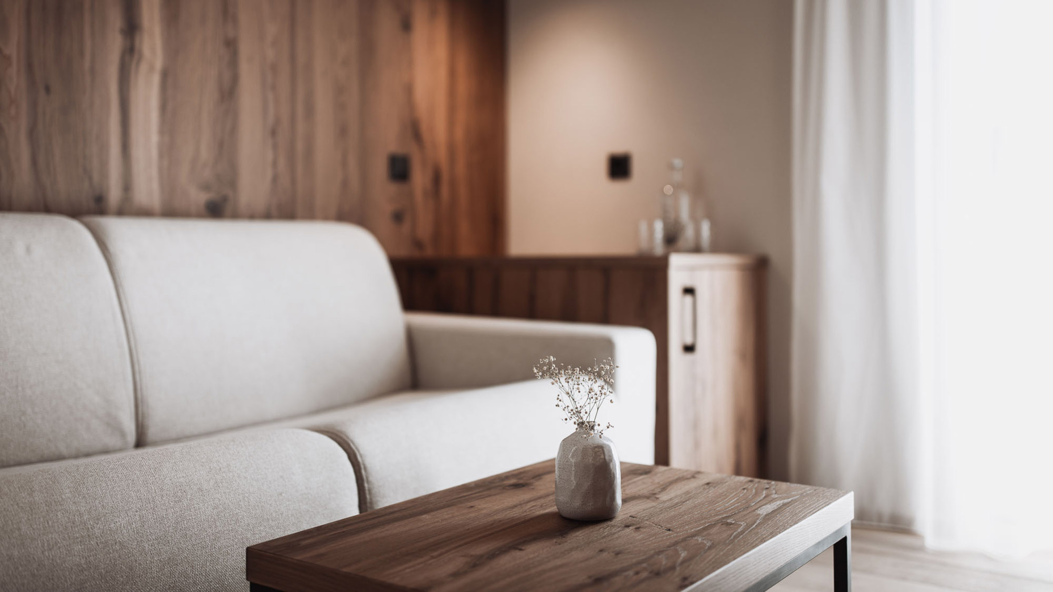 Light grey sofa and a wooden coffee table with a flower vase - Hotel Montis