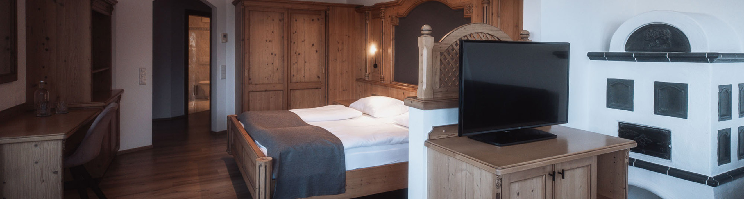 Schlafzimmer mit Doppelbett, Fernseher und Kachelofen der Turmsuite - Hotel Montis