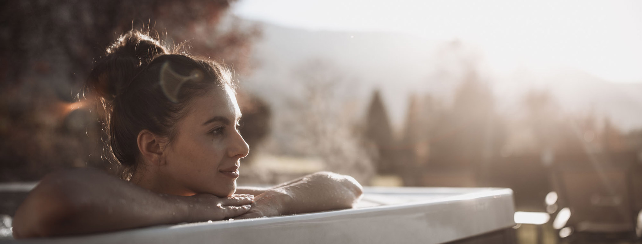 Eine Frau sitzt im Outdoor-Whirlpool und blickt in die Ferne - Hotel Montis