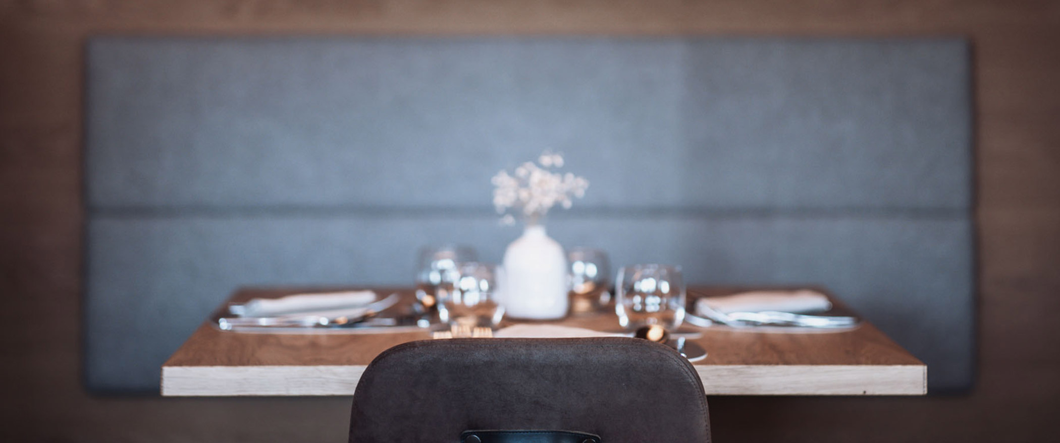 Seitenansicht auf einen gedeckten Tisch mit Sitzbank mit dunkelgrauer Polsterung - Hotel Montis