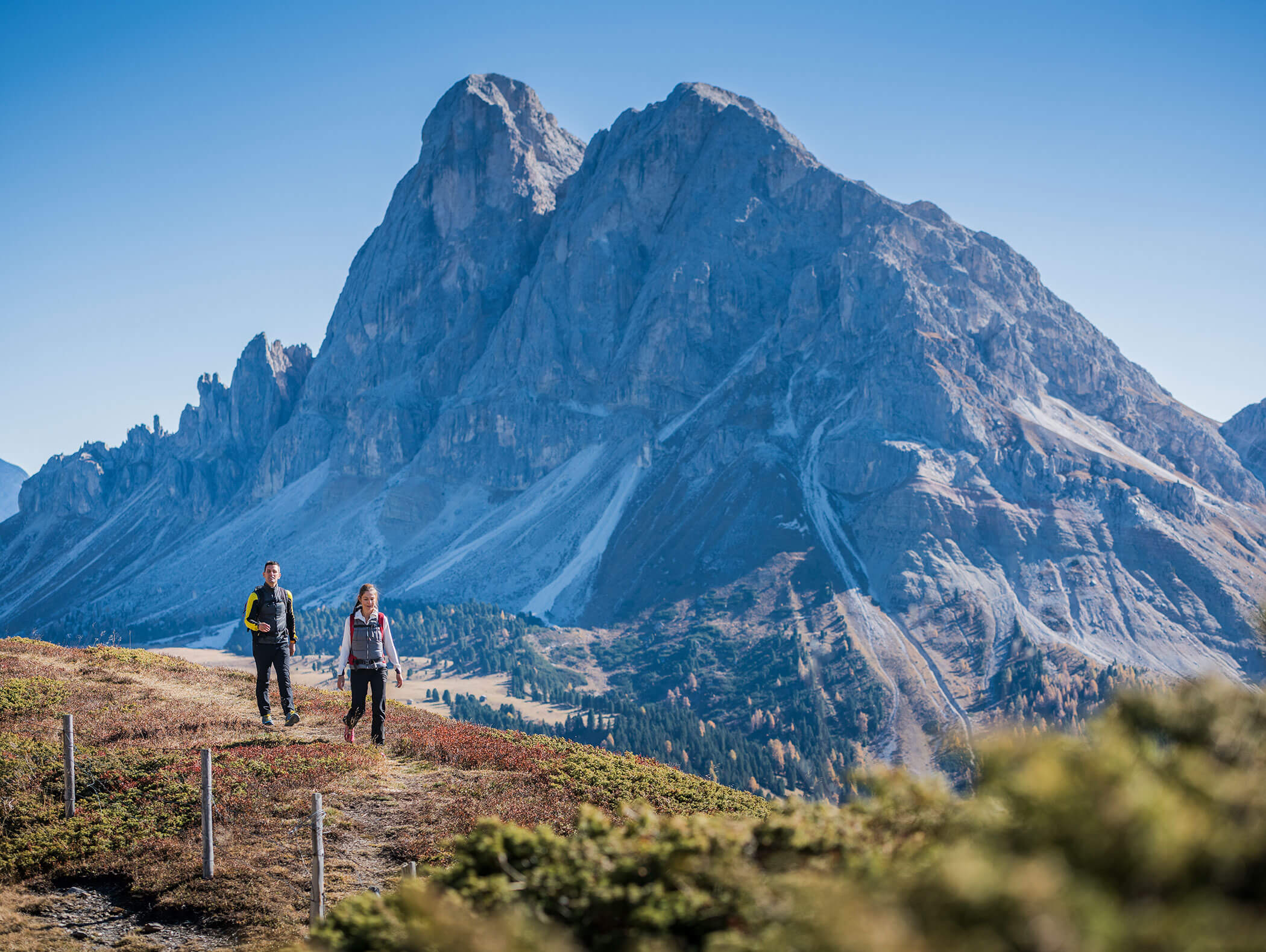 Zwei Wanderer unterwegs auf einem Almenpfad, dahinter die markanten Gipfel der Dolomiten - Hotel Montis